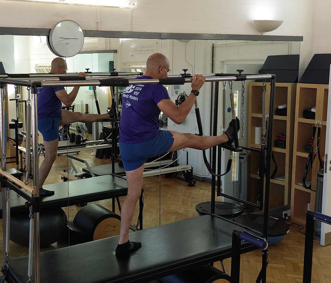 Teejay Sogunro demonstrating hamstring stretches on the Cadillac apparatus at The Sogunro Practice, London Colney, St Albans — Pilates for over 60s on the full STOTT apparatus.